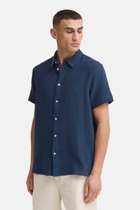 Blauw overhemd met korte mouwen van SOLID, met crêpe-achtige textuur, witte knopen, gedragen met een beige broek en zilveren armband.