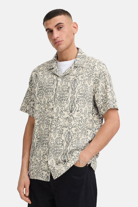 Ecru hemd met korte mouwen van SOLID, met zwart krullerig bloemenpatroon en reverskraag, gedragen over een wit T-shirt met zwarte broek.