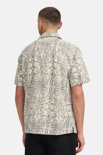 Chemise écru à manches courtes de SOLID, avec motif abstrait bouclé gris foncé, vue de dos avec un jean noir et un bracelet argenté.