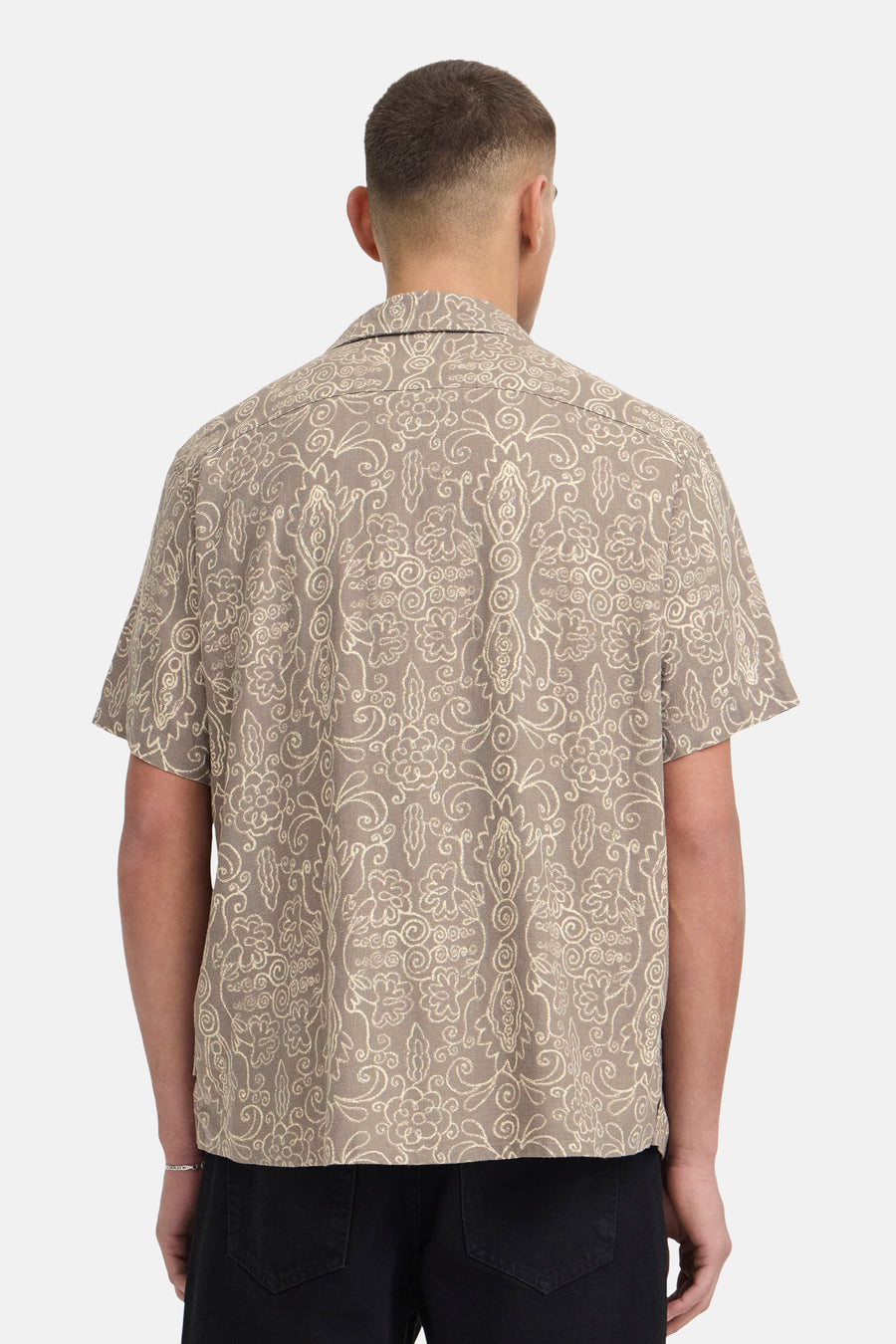 Bruin hemd met korte mouwen van SOLID, met off-white decoratief patroon, gedragen door een man van achteren gezien met zwarte broek en zilveren armband.