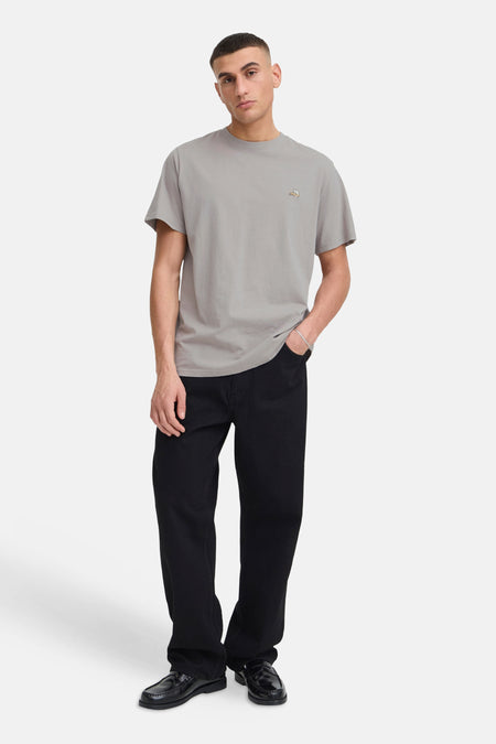 Taupe T-shirt met korte mouwen van SOLID met een geborduurd detail op de borst, gedragen met zwarte broek en loafers.