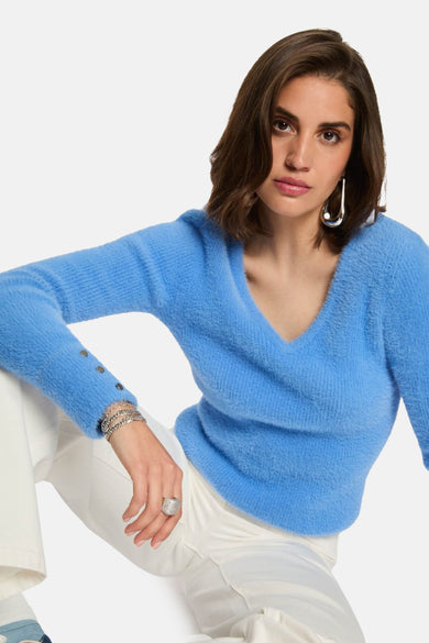 Pull à col V bleu de Morgan De Toi, avec longues manches et dos de short blanc et baskets.