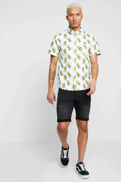 Zwarte denim jeansshort van ONLY & SONS® met opgerolde pijpen, gedragen met een ananasprint overhemd en zwarte sneakers, front view.