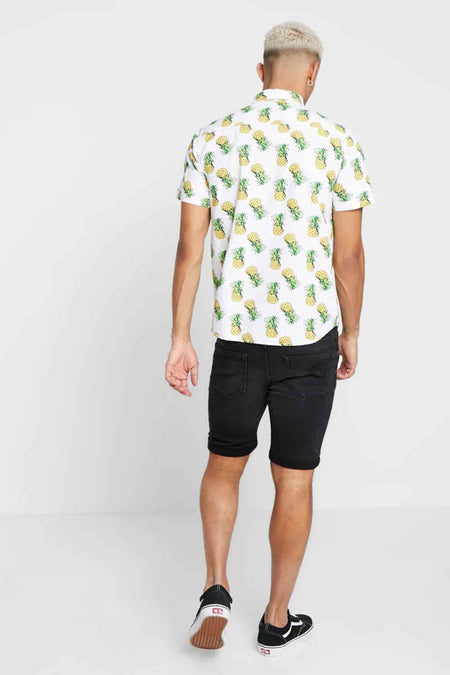 Zwarte denim jeansshort van ONLY & SONS®, achterzijde met opgerolde pijpen en zakken, gedragen met een witte ananasprint overhemd en zwarte sneakers.