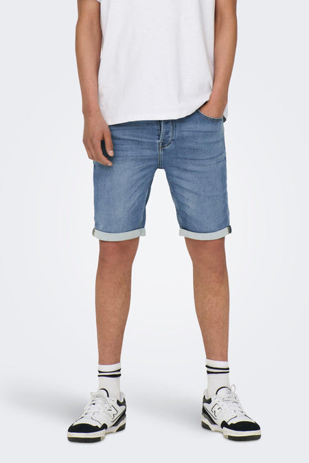 Jeansshort van lichtblauw denim van ONLY & SONS, met opgerolde pijpen, gecombineerd met een wit T-shirt, witte sokken en sneakers.