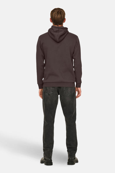 Bruine sweater met kap van ONLY & SONS®, met verder een donkere jeansbroek en zwarte schoenen.
