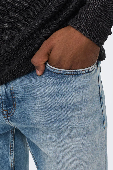 Lichtblauwe slim-fit jeans van ONLY & SONS® met gewassen denimtextuur en bruine naden, close-up van voorzak met hand erin