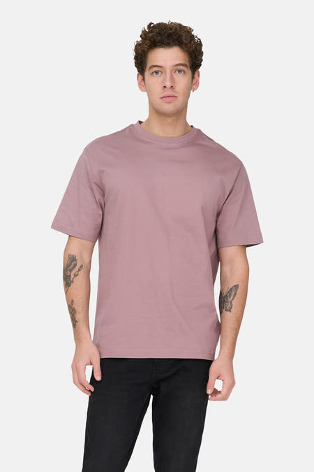 Roze T-shirt met korte mouwen van ONLY & SONS, met tatoeages op de armen, gecombineerd met een zwarte jeans.
