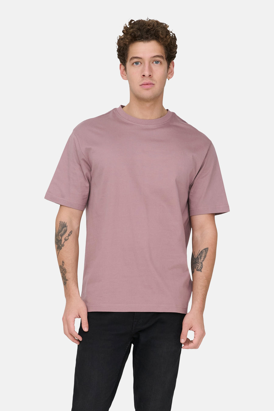 Roze T-shirt met korte mouwen van ONLY & SONS, met tatoeages op de armen, gecombineerd met een zwarte jeans.
