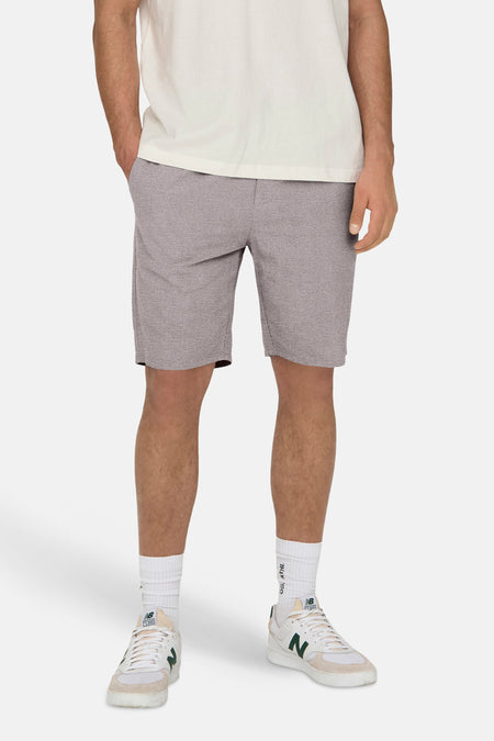 Grijze short van ONLY & SONS®, met steekzakken, gecombineerd met een wit T-shirt en witte sokken met sneakers.