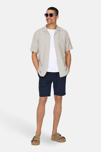 Beige overhemd met korte mouwen van ONLY & SONS, gedragen met een wit T-shirt, donkerblauwe korte broek en bruine sandalen.