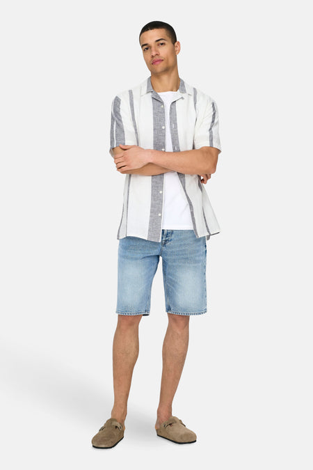 Ecrukleurig overhemd met korte mouwen van ONLY & SONS® met verticale strepen, gedragen over een wit T-shirt en lichtblauwe denim shorts.
