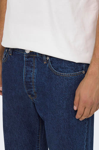 Donkerblauwe wide jeans van ONLY & SONS®, met gele stiksels en een witte T-shirt.
