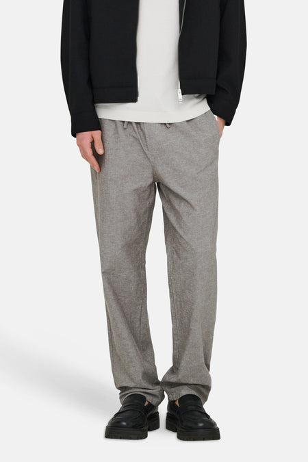 Pantalon marron ONLY & SONS® avec une texture légère, combiné avec un polo blanc et une veste noire, debout sur un fond blanc.
