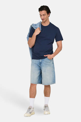 T-shirt bleu à manches courtes de ONLY & SONS, avec une veste en denim sur l'épaule, associé à des shorts en denim et des chaussettes blanches.