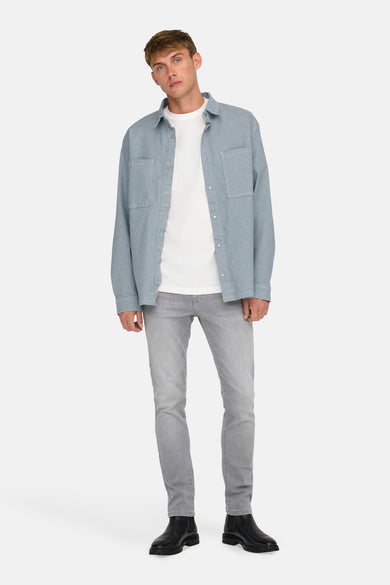 Lichtblauw denim overhemd met lange mouwen van ONLY & SONS, gedragen over een wit T-shirt en grijze jeans met zwarte laarzen.

