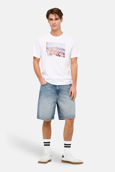 Jeansshort van denim in middenblauw van ONLY & SONS®, gedragen met een wit T-shirt en gestreepte sokken.
