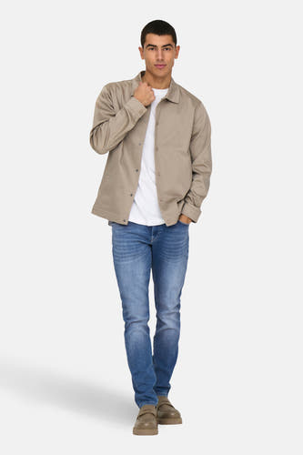 Jean slim fit en denim bleu de ONLY & SONS, associé à un t-shirt blanc et une veste beige.