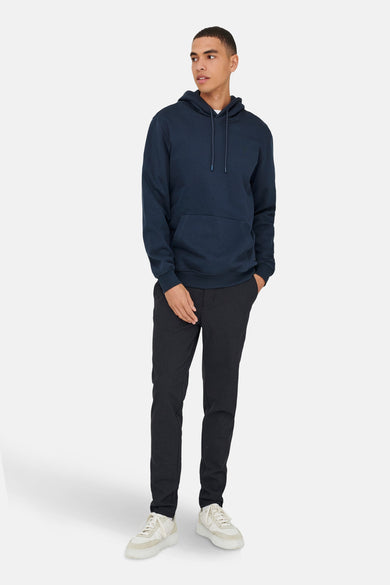 Blauwe sweater met kap van ONLY & SONS®, gecombineerd met donkere broek en witte sneakers.