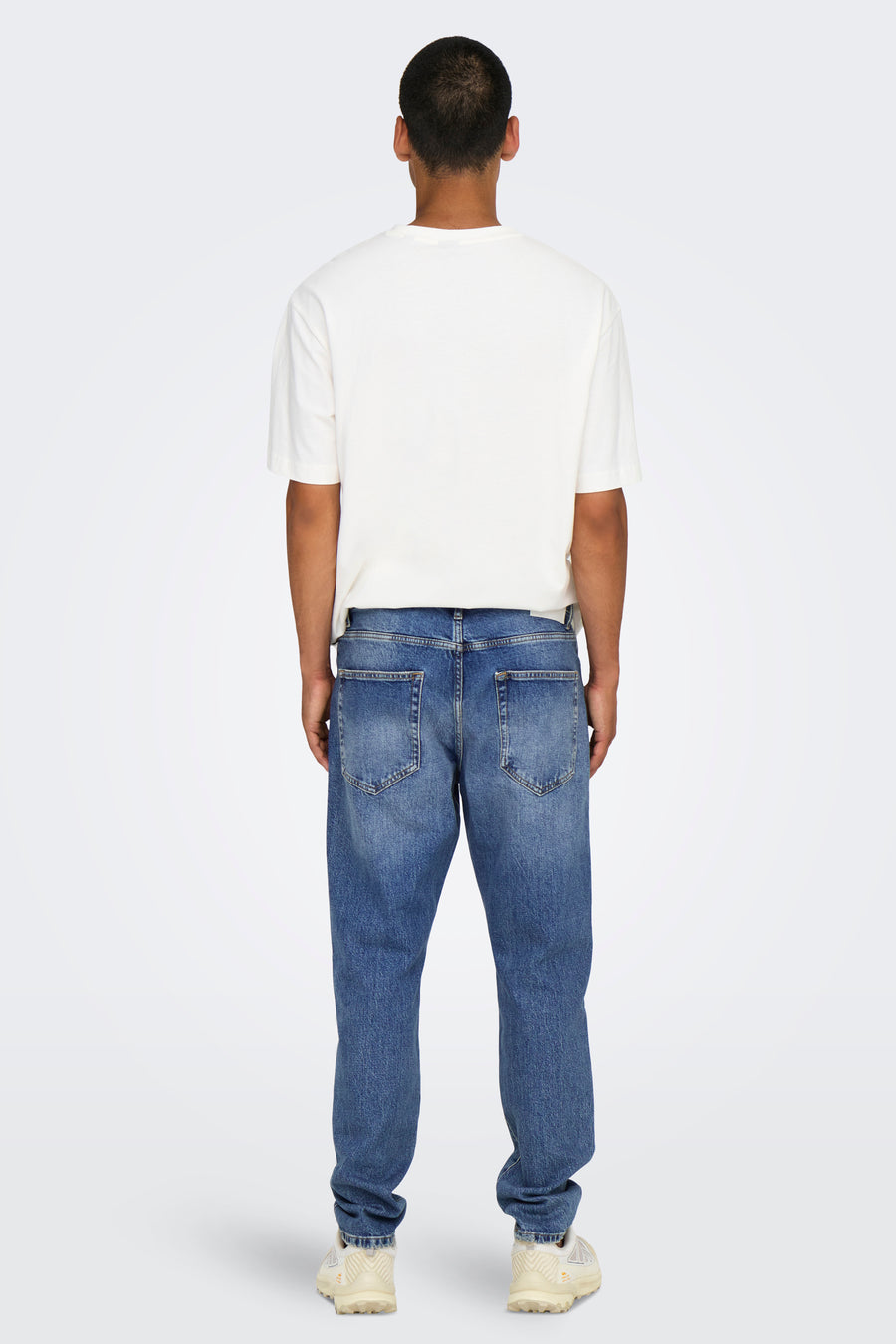Tapered jeans van midblauw denim van ONLY & SONS®, gezien van achteren, met een witte T-shirt en crèmekleurige schoenen.