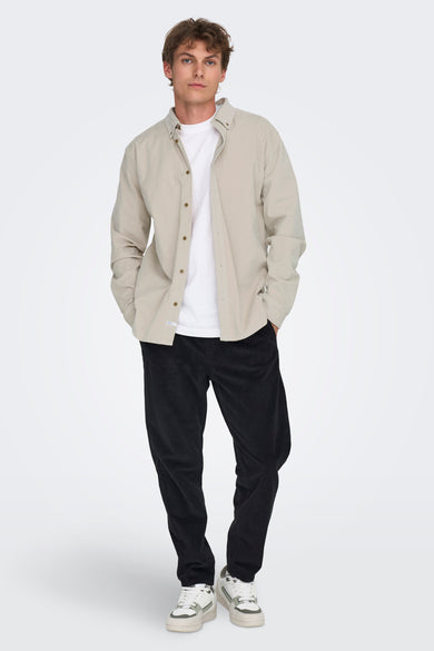 Ecrukleurig hemd met lange mouwen van ONLY & SONS®, gedragen over een wit T-shirt, met donkere corduroy broek en sneakers.
