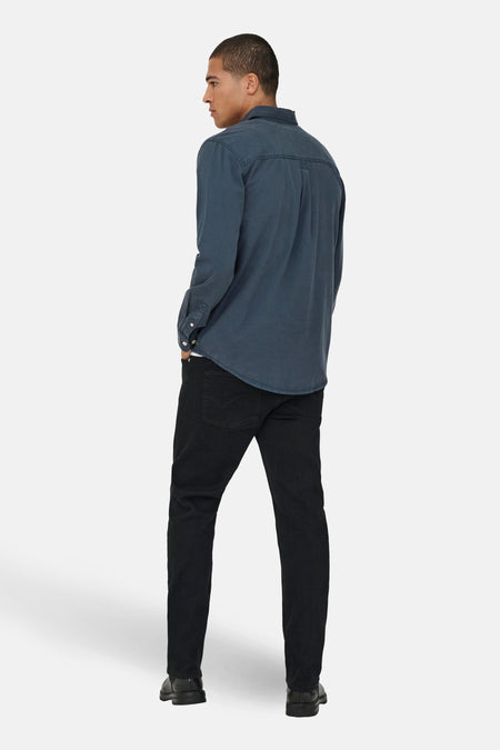 Een man van achteren gezien, in een blauw overhemd en zwarte broek.