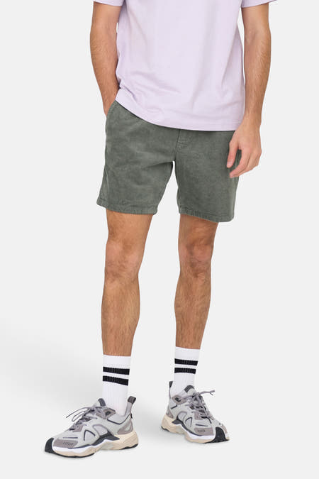 Short vert de ONLY & SONS, avec une texture en velours côtelé, porté avec des chaussettes blanches et des baskets grises.