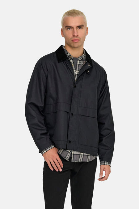 Zwarte korte jas van ONLY & SONS®, met knoopsluiting, corduroy kraag en een grijze geruite blouse eronder.

