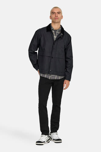 Zwarte korte jas van ONLY & SONS®, gedragen over een geruit overhemd met zwarte broek en witte sneakers.
