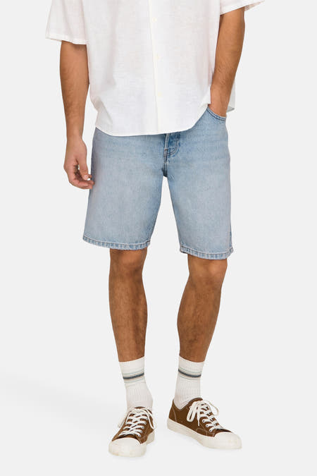 Jean court en denim bleu clair d'ONLY & SONS, avec un ourlet brut, porté avec une chemise en lin blanche et des chaussures marrons.