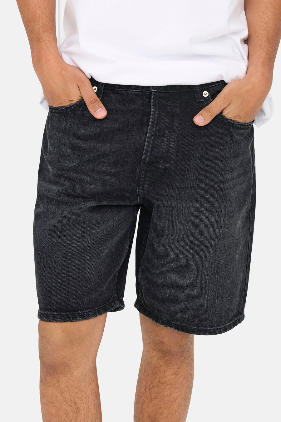 Short en jean noir ONLY & SONS®, avec main dans les poches et t-shirt blanc.