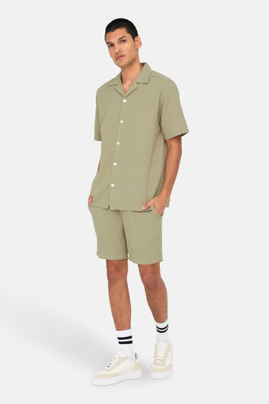 Beige short van ONLY & SONS, gedragen met een beige overhemd, witte sportschoenen en sokken met strepen.
