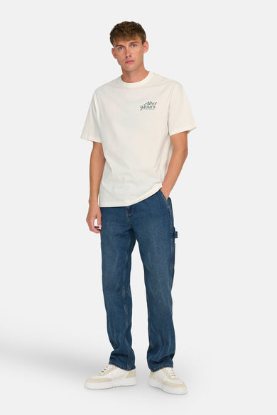 Ecru T-shirt met korte mouwen van ONLY & SONS®, met een kleine tekstprint en gecombineerd met blauwe jeans en crèmekleurige sneakers.
