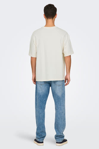 T-shirt blanc à manches courtes d'ONLY & SONS, avec une coupe décontractée, associé à des jeans bleus et des chaussures foncées.