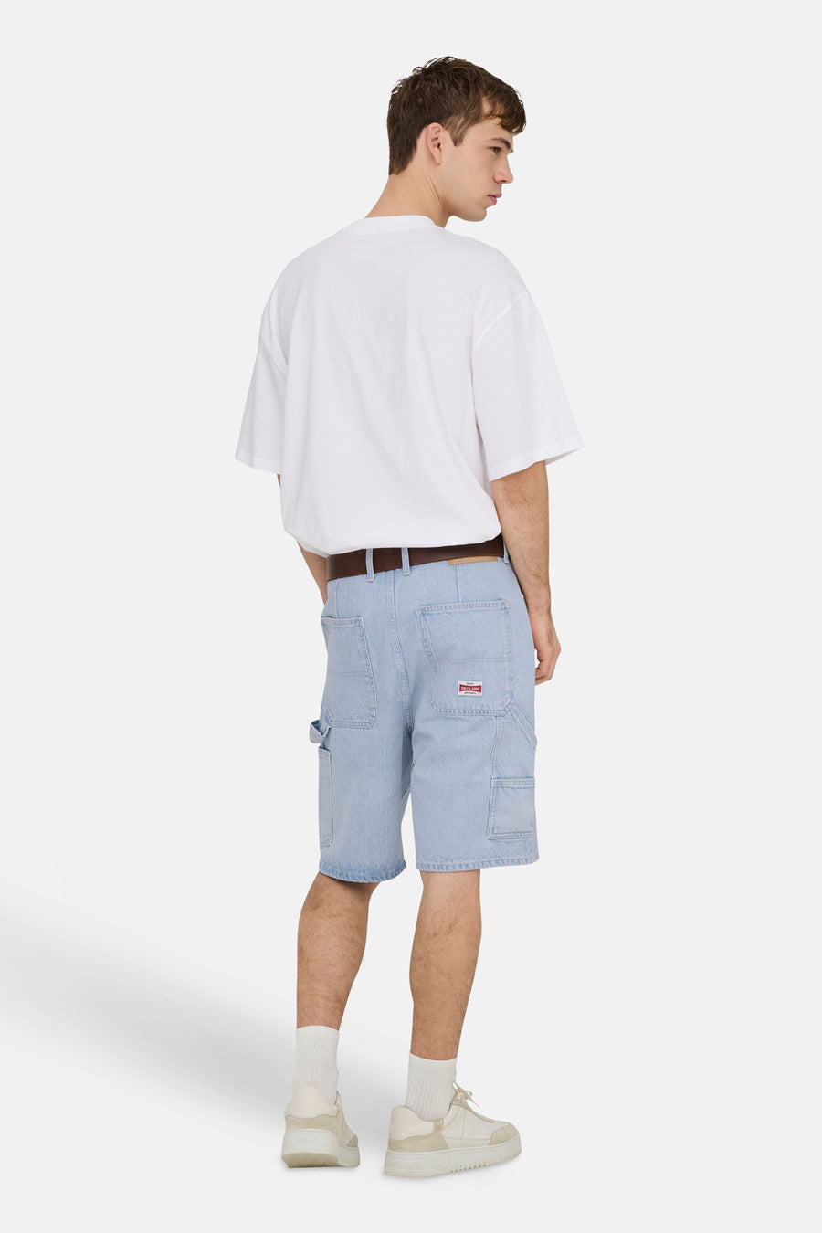 Short en jean bleu clair ONLY & SONS® avec poches utilitaires et écusson rouge, porté par un homme avec un t-shirt blanc et une ceinture, vu de dos.