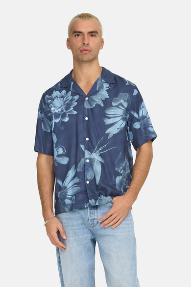 Chemise bleue à manches courtes de ONLY & SONS, avec un motif floral, portée avec des jeans.