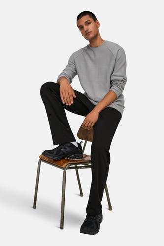 Zwarte broek van ONLY & SONS®, gecombineerd met een grijze trui en zwarte sneakers, zittend op een stoel.
