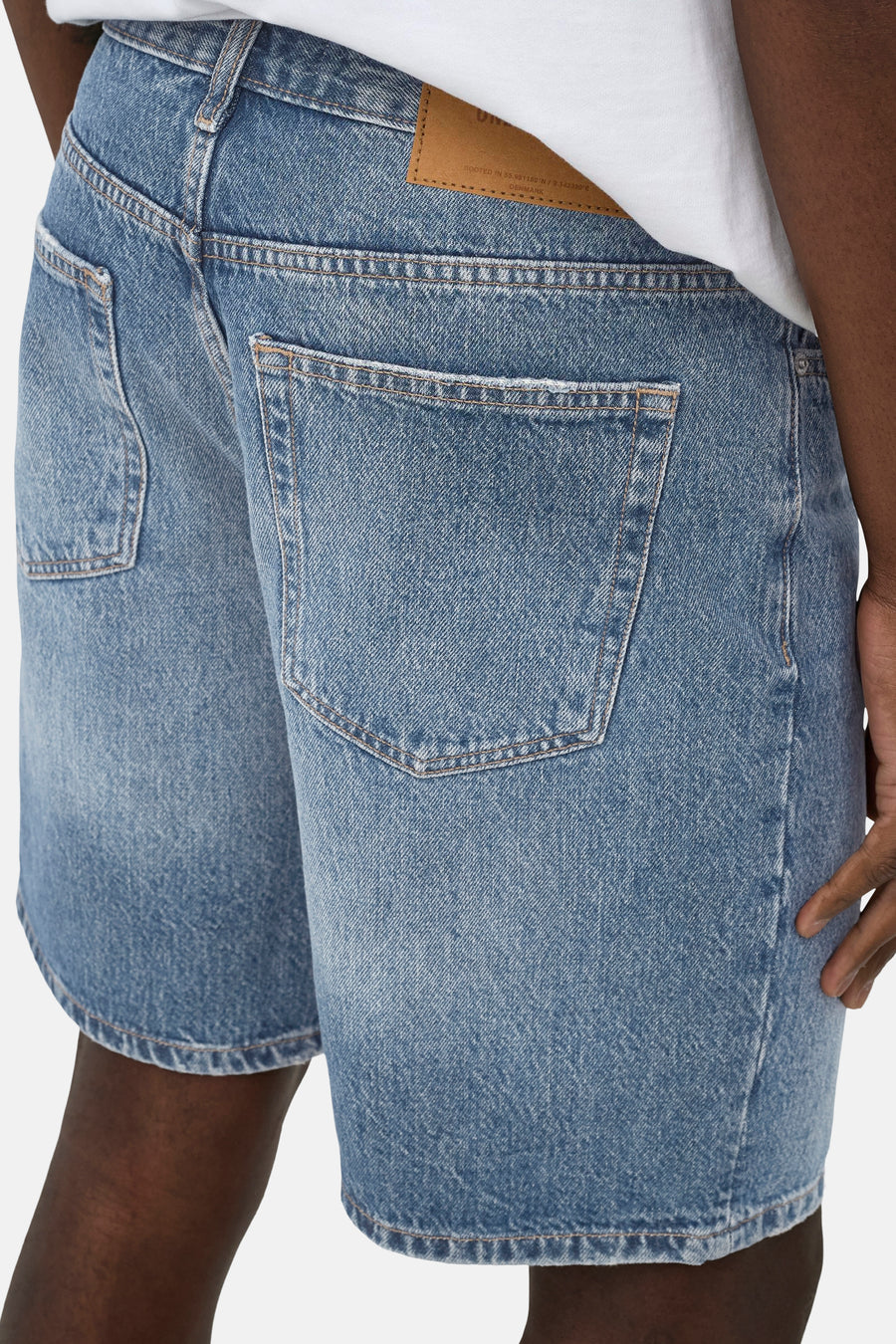 Middellichtblauwe jeansshort van ONLY & SONS, achterkant met zakken en leren merkpatch, gecombineerd met een wit t-shirt.