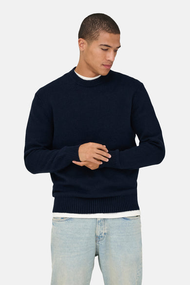 Blauwe trui met ronde hals van ONLY & SONS®, met lange mouwen en geribbelde details, gedragen met een wit T-shirt en jeans.
