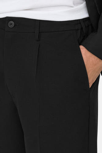 Pantalon noir de ONLY & SONS, avec une main dans la poche et un nœud visible.