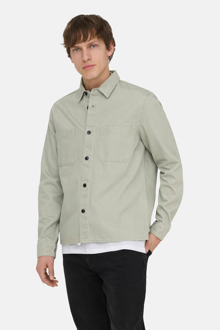 Groen hemd van ONLY & SONS®, met lange mouwen, knoopsluiting en borstzakken, gedragen over een wit T-shirt en een zwarte jeans.
