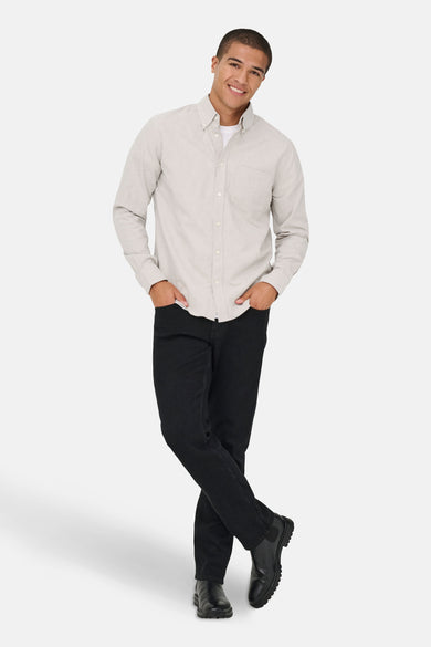 Chemise beige à longues manches de ONLY & SONS, portée avec un t-shirt blanc, des jeans noirs et des bottes en cuir.