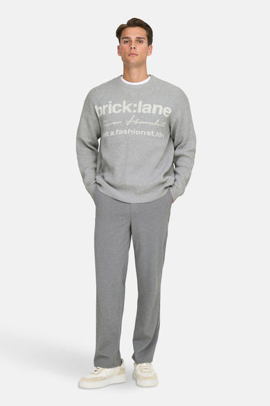Sweat gris à col rond de ONLY & SONS®, avec un slogan sur la poitrine, associé à un t-shirt blanc et un pantalon gris.