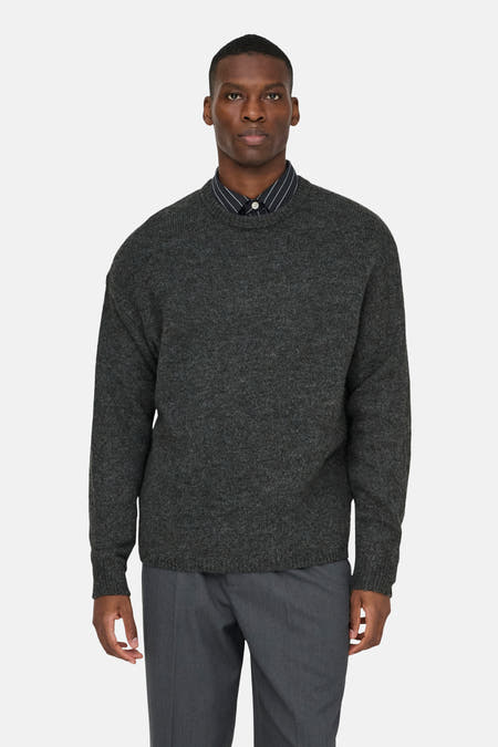 Sweat gris à col rond de ONLY & SONS®, porté sur une chemise rayée et un pantalon gris.