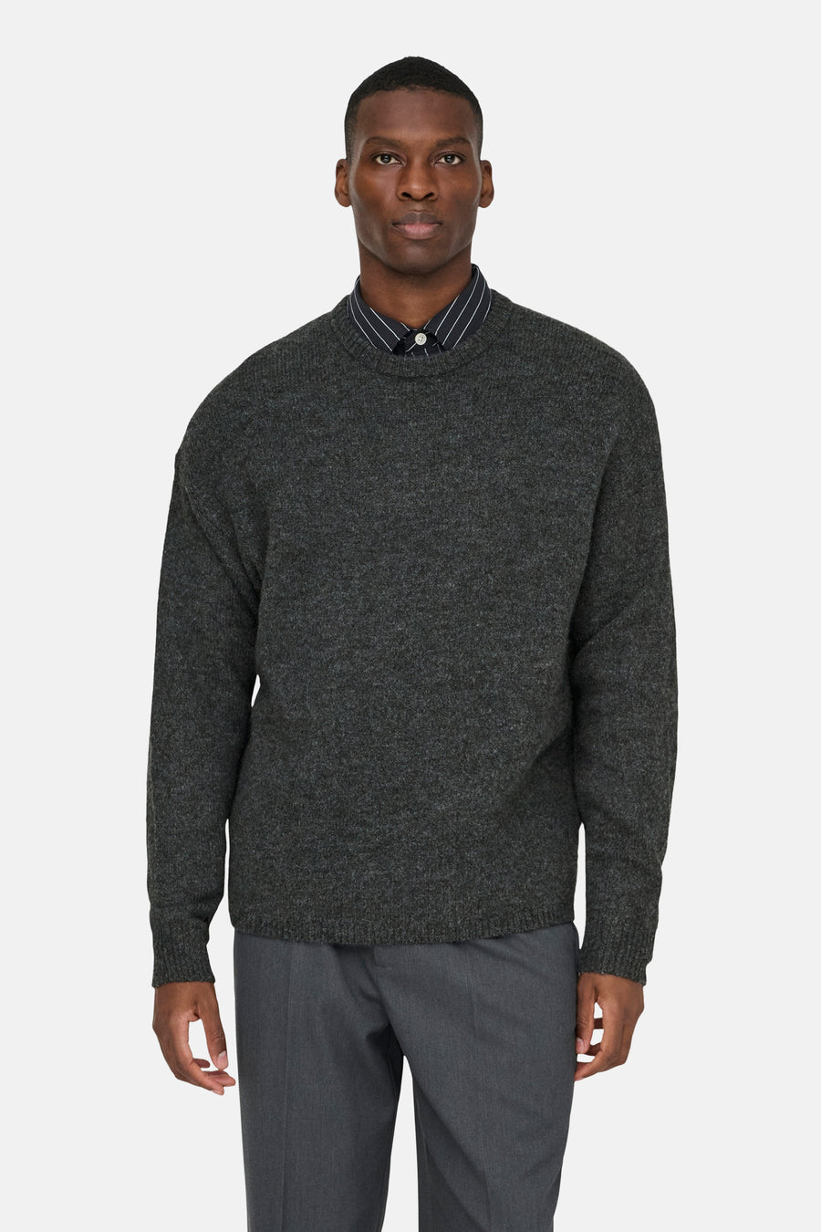 Sweat gris à col rond de ONLY & SONS®, porté sur une chemise rayée et un pantalon gris.