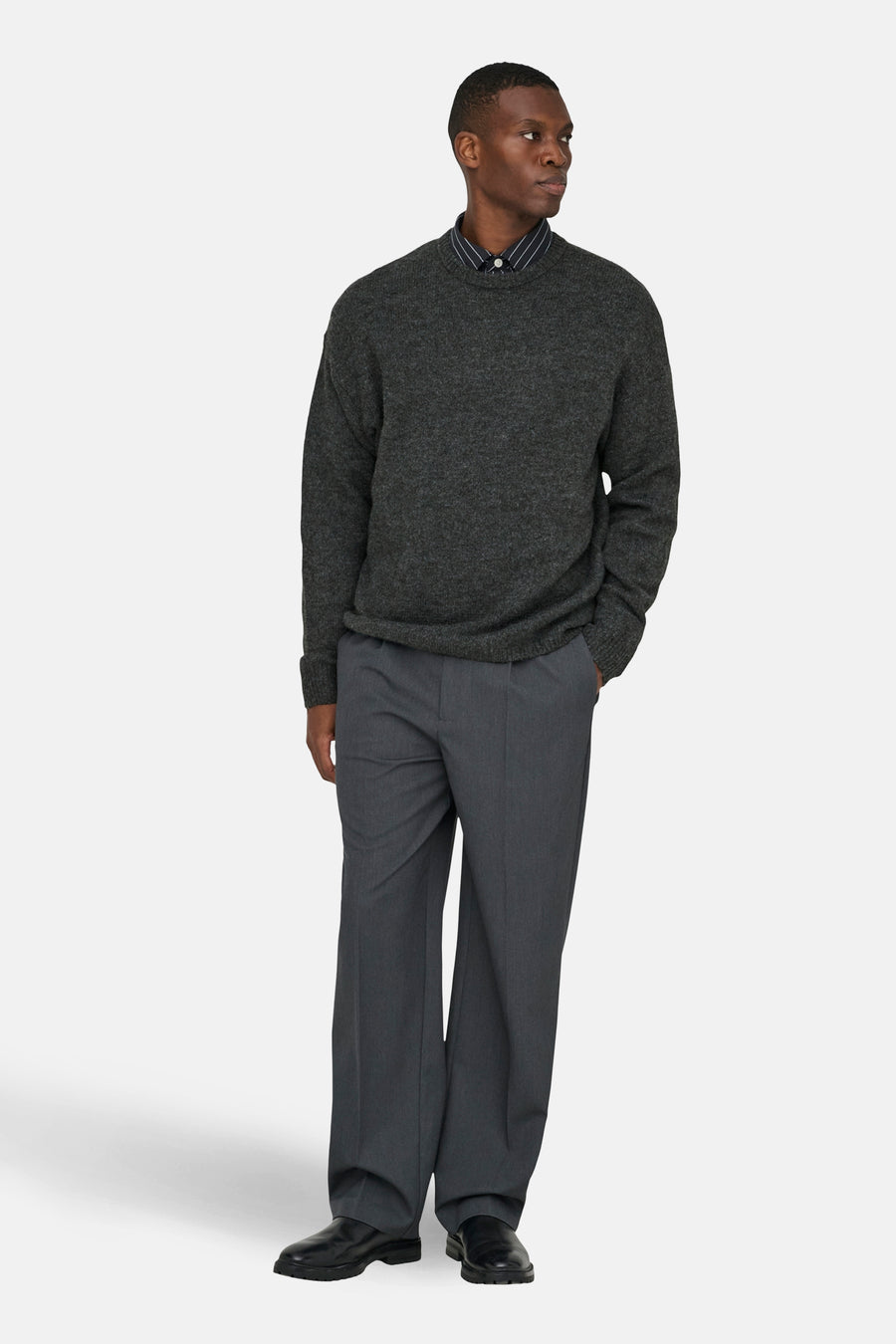 Grijze trui met ronde hals van ONLY & SONS®, gedragen over een gestreept overhemd en grijze pantalon.
