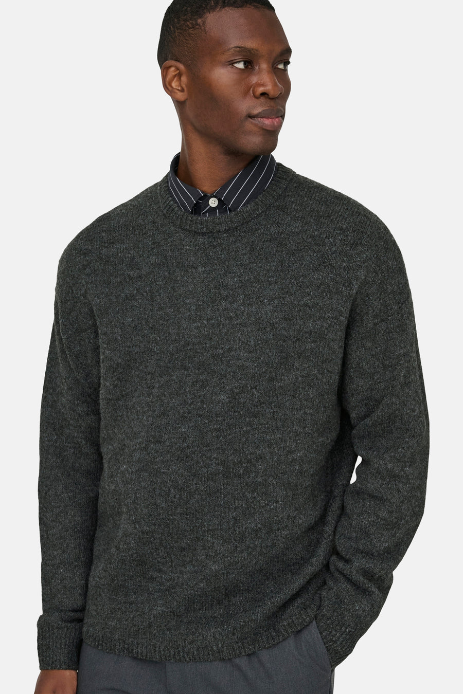 Sweat-shirt gris avec col rond de ONLY & SONS®, porté sur une chemise à rayures, contre un fond uni.
