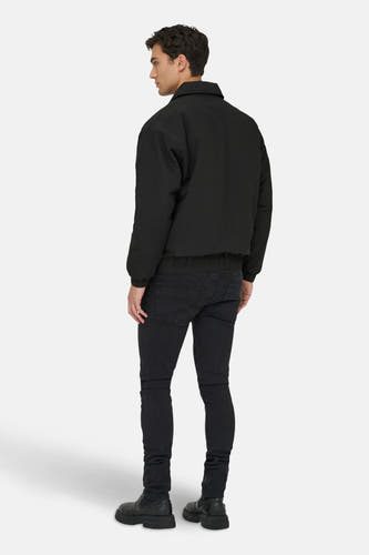 Zwarte jas van ONLY & SONS, met lange mouwen, gecombineerd met een donkere jeans en zwarte schoenen.
