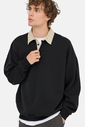 Pull-over noir de ONLY & SONS®, avec col et fermeture à boutons, porté sur une chemise blanche et un pantalon à carreaux.
