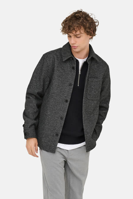 Grijs shirt met lange mouwen van ONLY & SONS, met knoopsluiting, gedragen over een zwarte trui en grijze pantalon.
